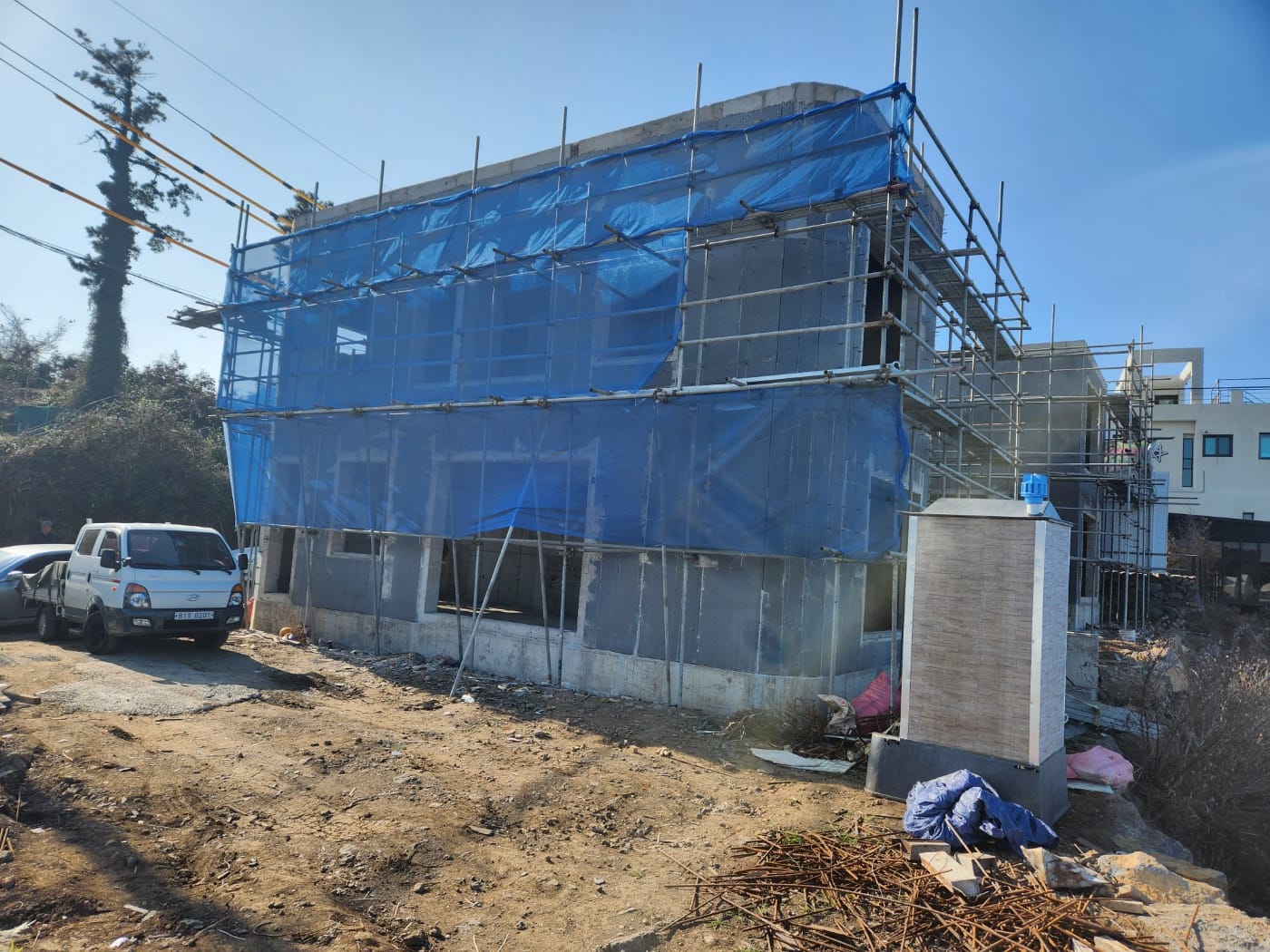 Two-storey concrete shell wrapped in blue safety mesh