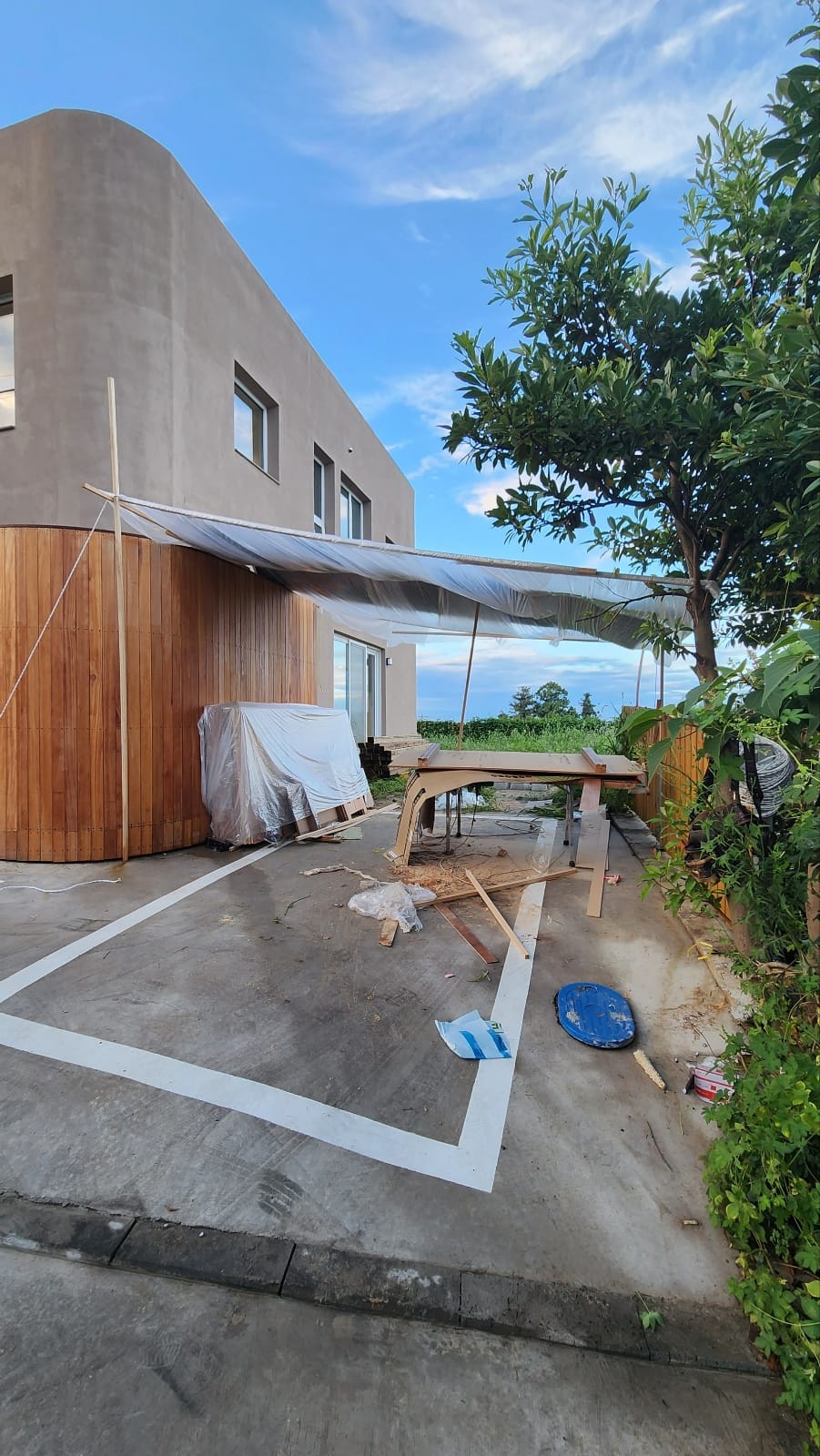 Carpentry work sheltered under plastic sheeting beside the rendered house in the rain